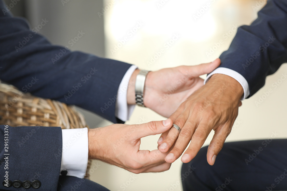 Gay man putting wedding ring on his partner's finger, closeup