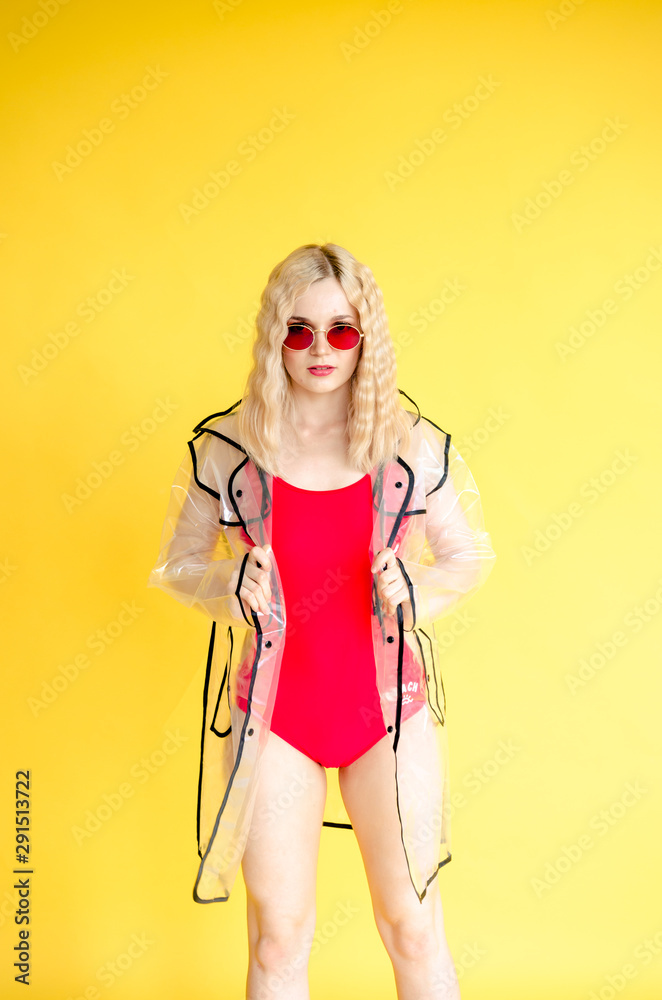 Stylish young girl in red swimsuit and transparent raincoat on yellow background Stylish young girl in red swimsuit and transparent raincoat on yellow background