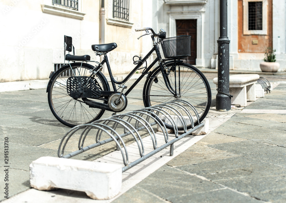 Black bike mounted on a bicycle stand on italian street.