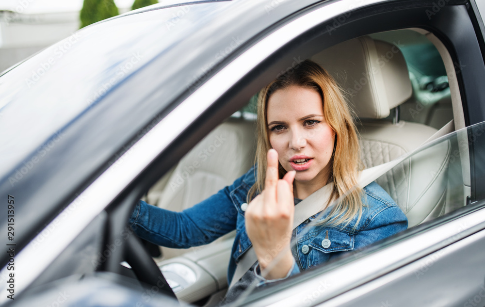 Angry young woman driver sitting in car, showing middle finger. Angry young woman driver sitting in car, showing middle finger.