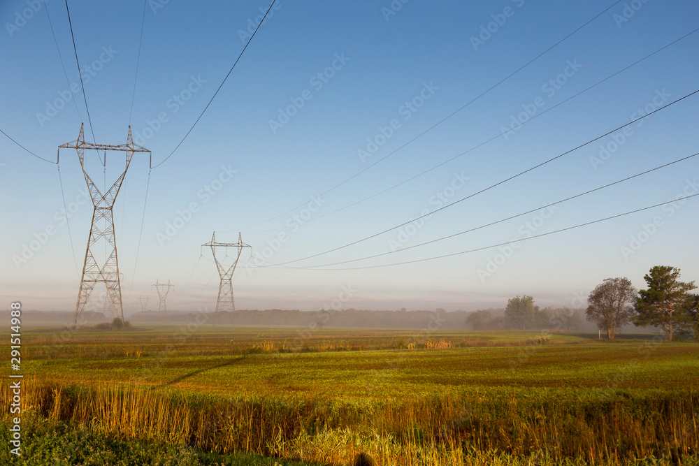 View of power line towers in farmland fields during a beautiful misty late summer golden hour morning, St.-Charles-de-Bellechasse, Quebec, Canada View of power line towers in farmland fields during a beautiful misty late summer golden hour morning, St.-Charles-de-Bellechasse, Quebec, Canada
