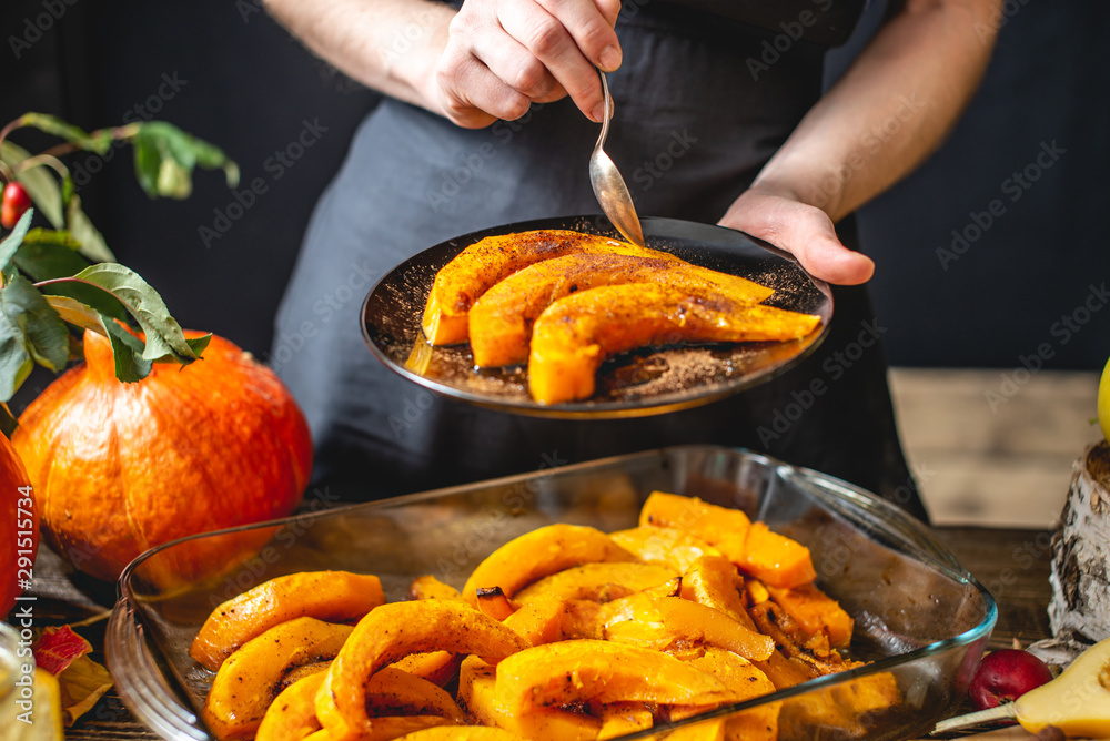 Woman chef holding slices of baked orange pumpkin with honey and cinnamon. Autumn food in a cozy kitchen. Close up