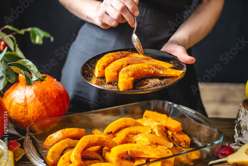 Woman chef holding slices of baked orange pumpkin with honey and cinnamon. Autumn food in a cozy kitchen. Close up