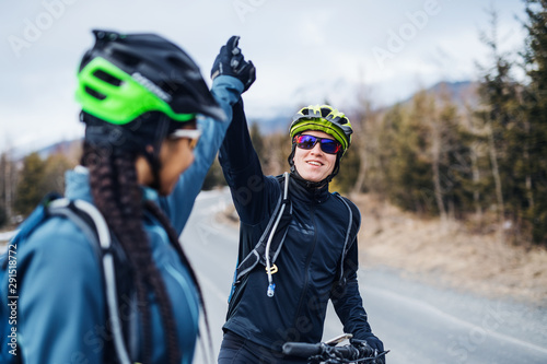 Two mountain bikers standing on road outdoors in winter, giving high five.