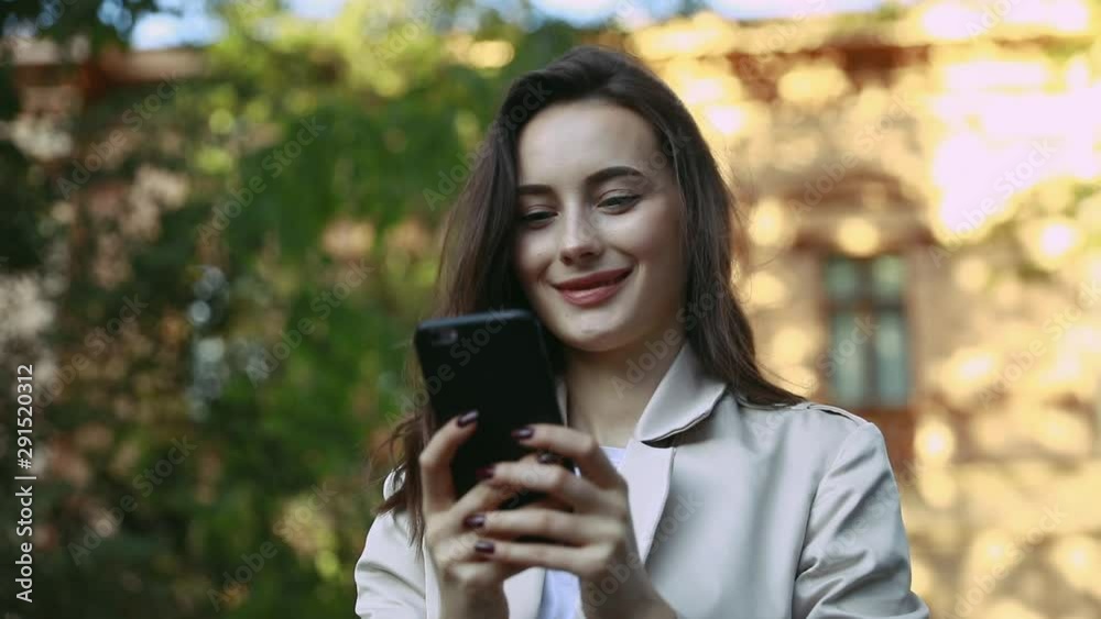 Adult Caucasian Confident Young Business Woman is Using Smartphone App Outside near park. Slow Motion Corporate Shot with Moving Camera Around Adult Caucasian Confident Young Business Woman is Using Smartphone App Outside near park. Slow Motion Corporate Shot with Moving Camera Around