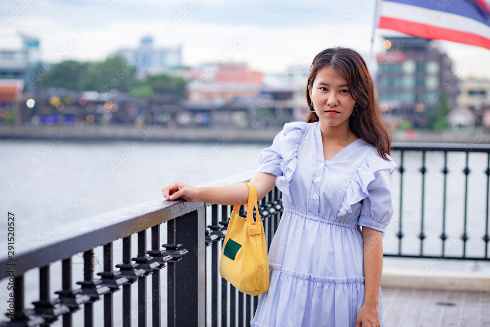 Beautiful Asian woman in light blue dress carrying a small yellow tote bag standing at the riverside