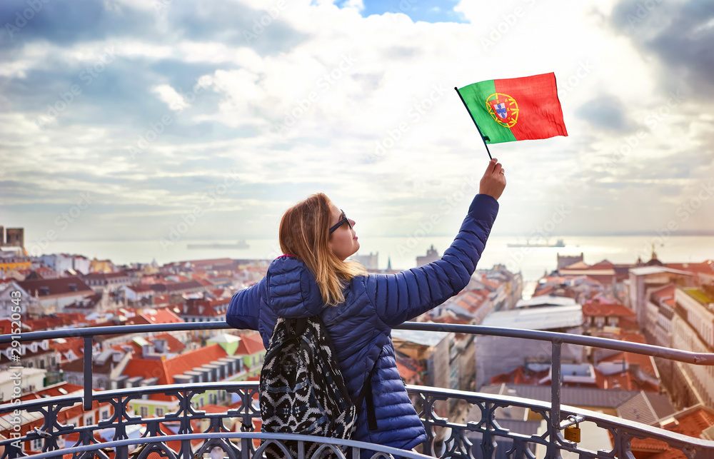 Young woman tourist enjoying beautiful cityscape top view on the old town holding the flag of Portugal in hands during the sunny day in Lisbon city - obrazy, fototapety, plakaty 
