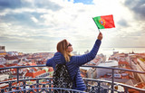 Young woman tourist enjoying beautiful cityscape top view on the old town holding the flag of Portugal in hands during the sunny day in Lisbon city