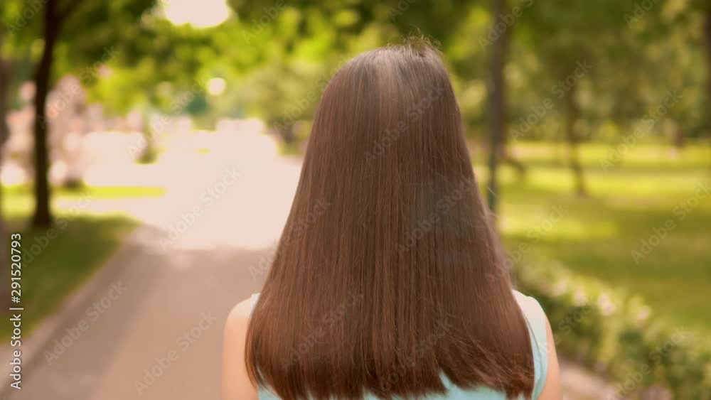 businesswoman turn head looking camera walks on pedestrian zone along alley with green trees cheerful brunette girl strolls outdoors summer nature background