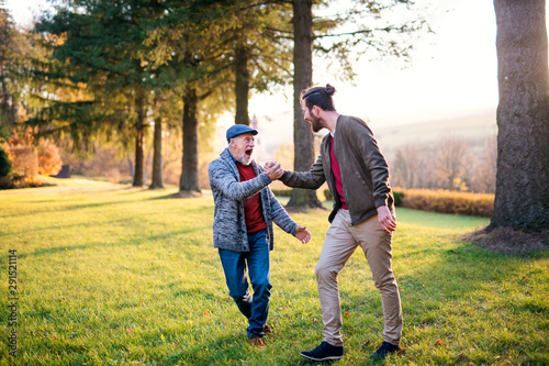 Laughing senior father and his son on walk in nature  shaking hands.