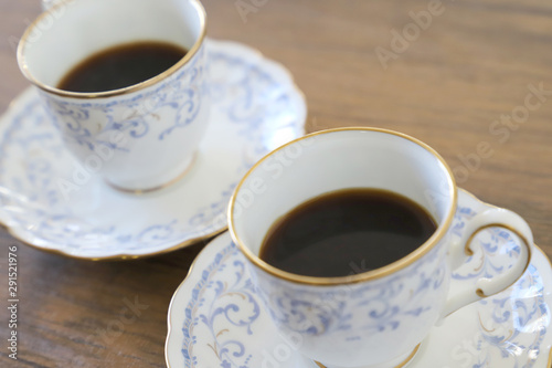 木製テーブルの上に乗った白い陶器のカップ&ソーサーにブラックコーヒー