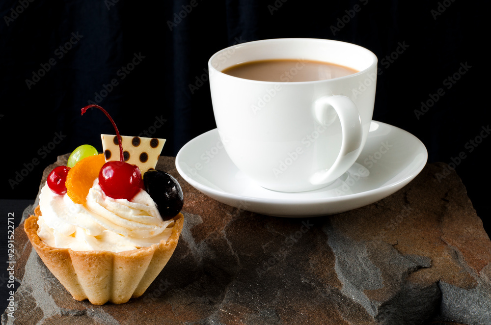 Fruit cake with cherries, grapes and plum stands on a wild stone next to a white cup of coffee with a foam Fruit cake with cherries, grapes and plum stands on a wild stone next to a white cup of coffee with a foam