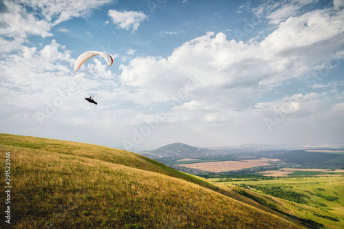 A white-orange paraglider flies over the mountainous terrain