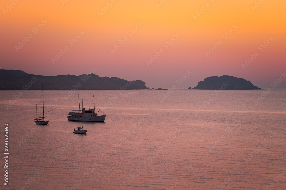 Boats seeing the sunset at August in Cavalleria beach at the north coast of Menorca, Spain.