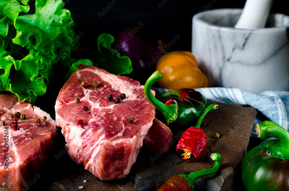 Two juicy steaks lie on a wild stone next to red and green chili peppers and a fresh green salad on a black wooden table