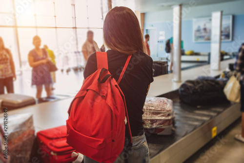 A girl with a red backpack is waiting for her luggage at the airport photo