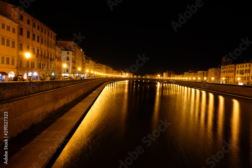 Illuminated shores on the river Arno in Pisa at night, dark and lively location for summer nightlife, used by students, tourists and young people, long exposure shot, copy space