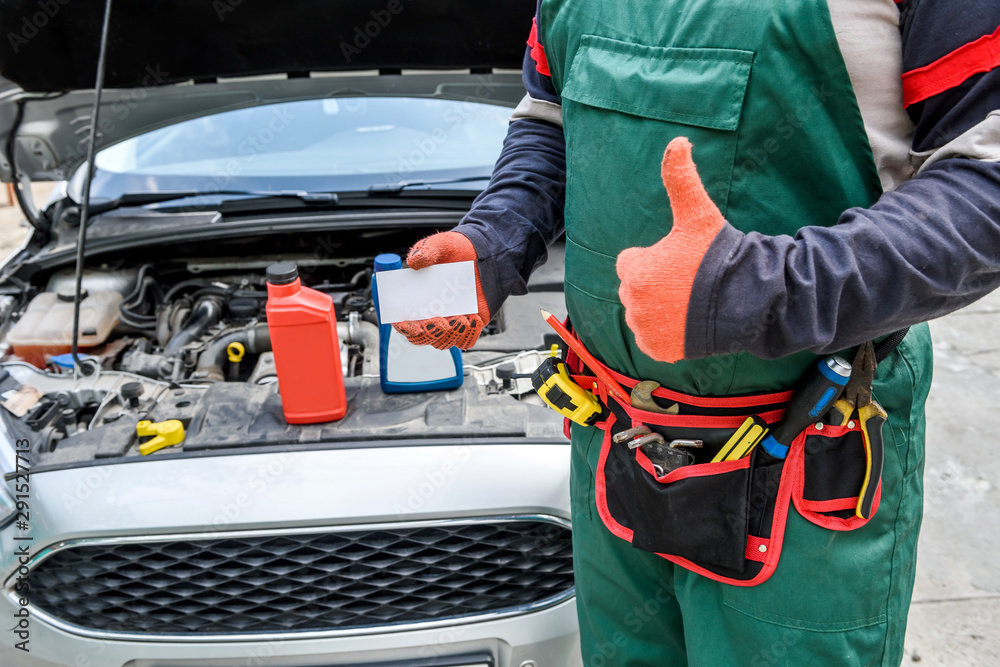Fototapeta premium Mechanic with visit card posing near car with open hood