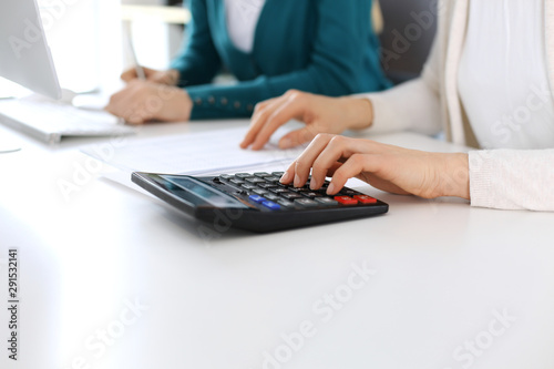 Accountant checking financial statement or counting by calculator income for tax form  hands close-up. Business woman sitting and working with colleague at the desk in office. Audit concept.