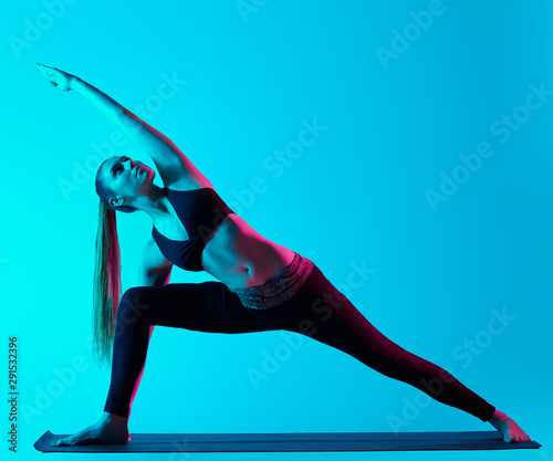 one caucasian woman exercising Utthita Parsvakonasana yoga exercices in silhouette studio isolated on blue background