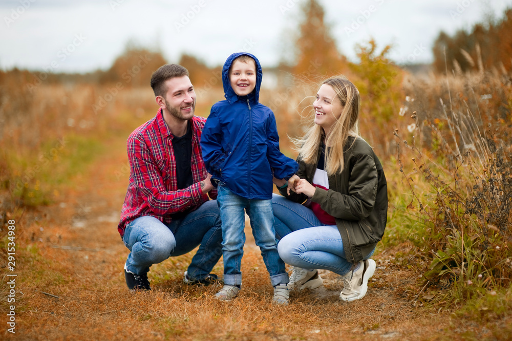 Young parents, smiling, look at their son. Family in casual clothes in the countryside Young parents, smiling, look at their son. Family in casual clothes in the countryside