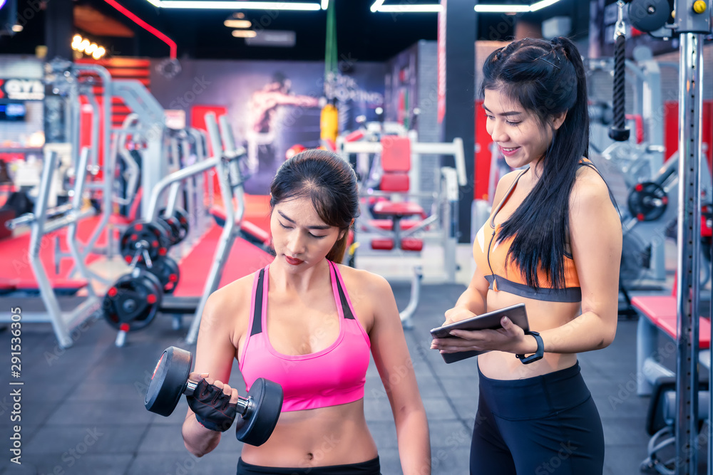 Fitness, sport, training and lifestyle concept - Young women flexing muscles in fitness gym center.