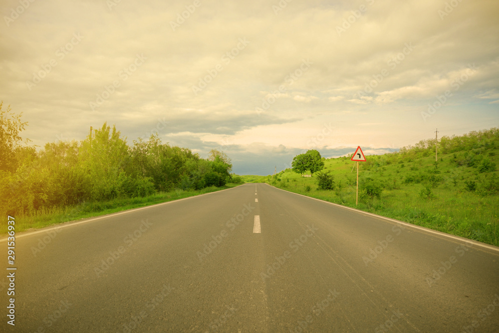 Road sign indicating left turn, blue sky with clouds and green trees Road sign indicating left turn, blue sky with clouds and green trees