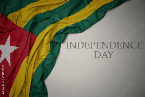 waving colorful national flag of togo on a gray background with text independence day.