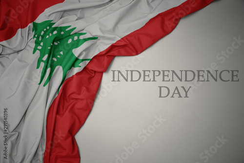 waving colorful national flag of lebanon on a gray background with text independence day.