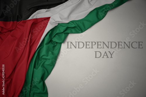 waving colorful national flag of palestine on a gray background with text independence day.