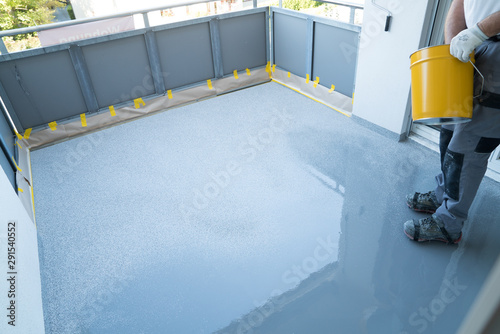 construction worker renovates balcony floor and spreads chip floor covering on resin and glue coating before applaying water sealant