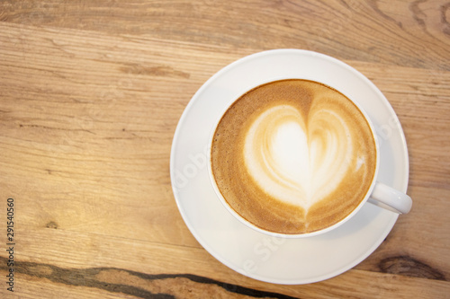 Heart-shaped foam coffee in white cup & saucer on wooden table 