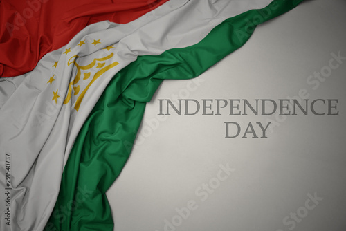 waving colorful national flag of tajikistan on a gray background with text independence day.