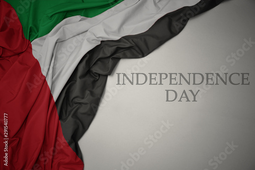 waving colorful national flag of united arab emirates on a gray background with text independence day.