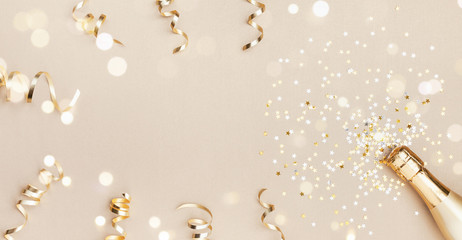 Champagne bottle with confetti stars, bokeh decoration and party streamers on golden background. Christmas, birthday or wedding concept. Flat lay.