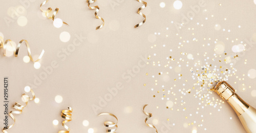 Champagne bottle with confetti stars, bokeh decoration and party streamers on golden background. Christmas, birthday or wedding concept. Flat lay.