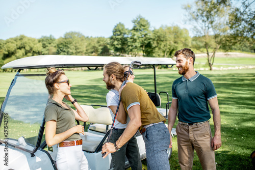 Group of a young happy friends gathering together before the golf game near the car on a playing course on a sunny day