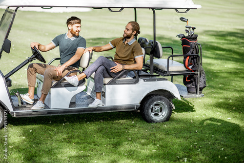 Two male best friends having fun while driving a golf car on the playing course on a sunny day