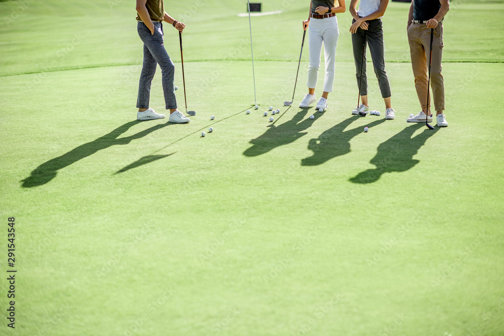 Obraz premium People practising golf, standing near the golf hall with balls and putters on a playing course outdoors, cropped image with shadows and no face