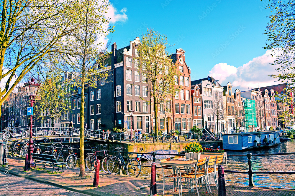 The typical Amsterdam street in sunny spring evening. Bicycles parked on a bridge in the channel, Netherlands.