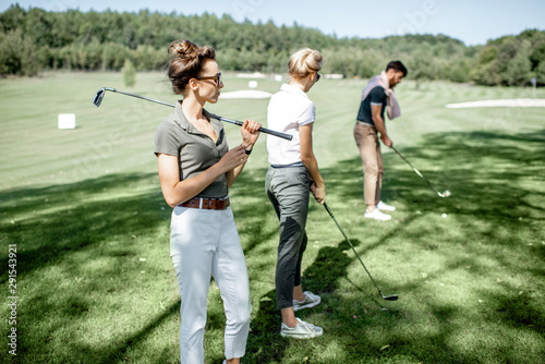 Portrait of an elegant young woman standing with golf putter and friends playing golf on the background