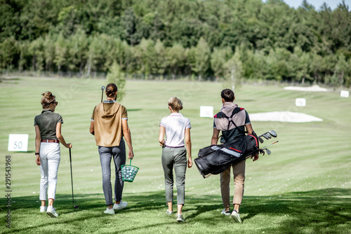 Young and elegant friends walking with golf equipment, hanging out together before the golf play on the beautiful course on a sunny day, rear view