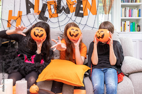 Happy cute children boy and girls in costume on sofa in living room during Halloween party, with pumpkin Jack-o'-lantern cover face