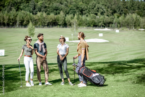 Young and elegant friends standing together with golf equipment, having fun during a golf play on the beautiful course on a sunny day