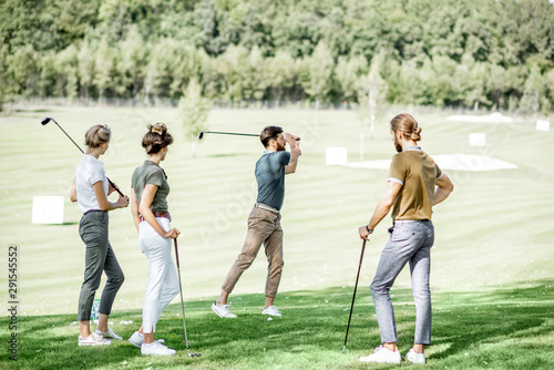 Group of a young people dressed casually playing golf on the beautiful golf course on a sunny day, man swinging a putter