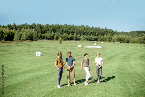 Portrait of a young group of friends standing with golf equipment on the golf course during a game on a sunny day, wide landscape view