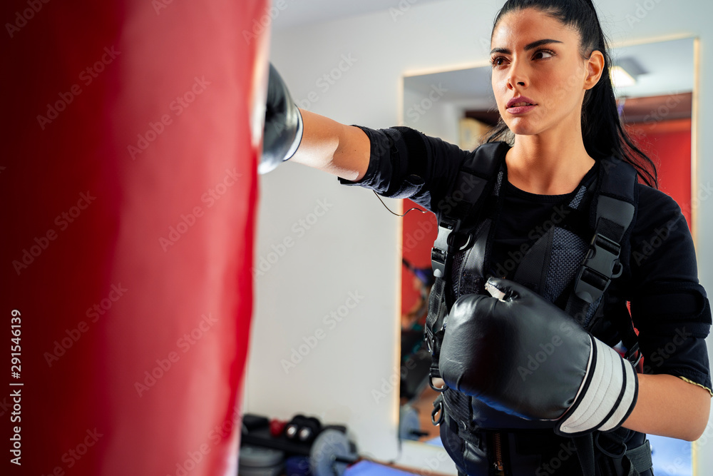 Closeup shot attractive strong female boxer punching bag in ems suit 