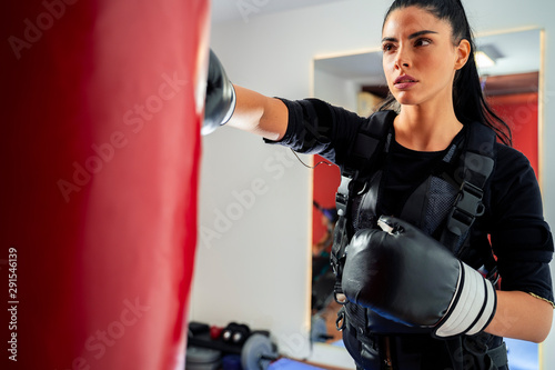 Closeup shot attractive strong female boxer punching bag in ems suit  © phoenix021