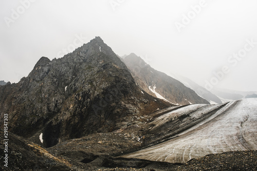 A high peramidal mountain near a melting glacier. The rocky slopes are covered with snow. Volumetric photo of Altai. Sharp peaks are hidden by impenetrable fog. The beginning of mountain rivers. photo