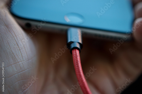 Male hand holding a charging smartphone with a red lead